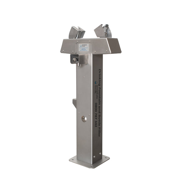 Mount Edgecumbe outdoor drinking fountain with clear water flowing, surrounded by greenery under blue sky.